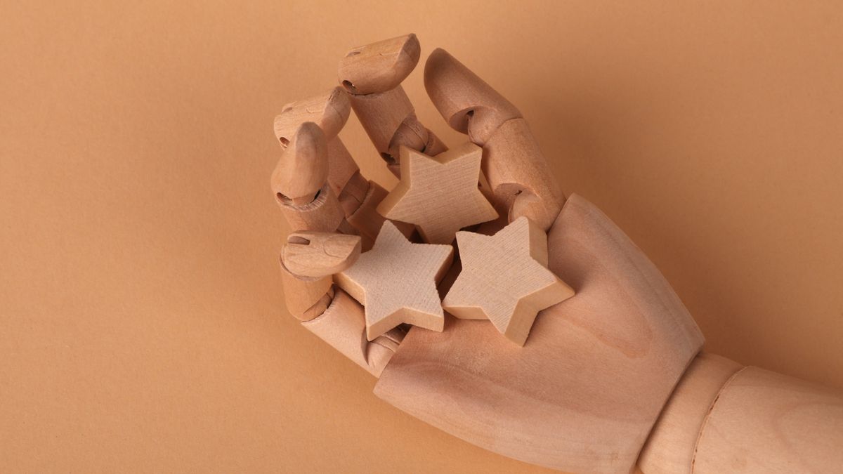 Mano de maniquí de madera sosteniendo tres estrellas de madera sobre fondo beige