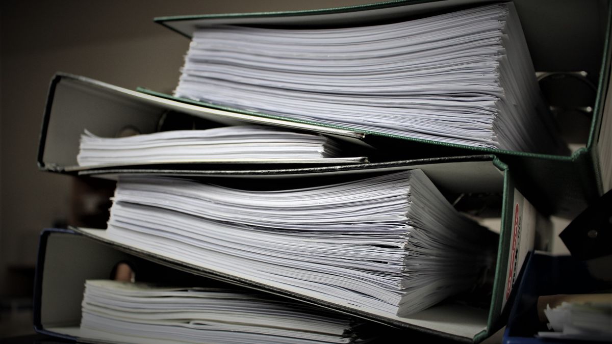 Stack of open ring binders crammed with loose sheets of paper piled on top of each other