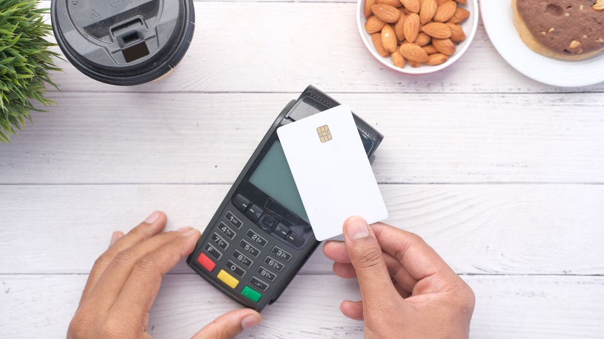 Hands holding a chip card over a card payment terminal, seen from above on a white table