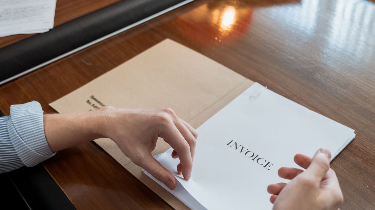 Hands on a wooden desk turning the pages of a printed invoice next to a brown envelope