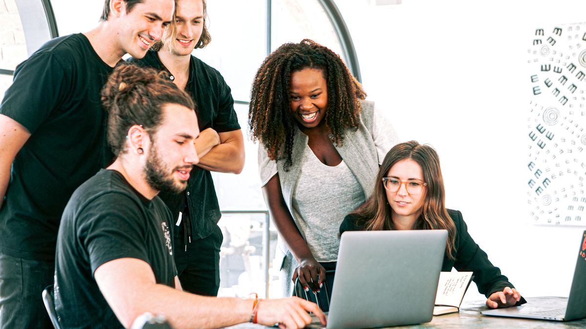 Five colleagues gathered around a table looking at a laptop screen while one of them types