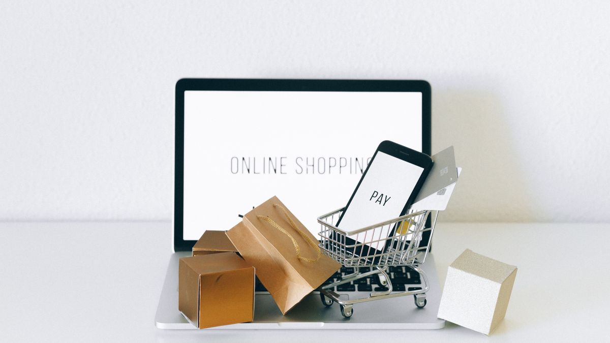Portátil con la frase online shopping en pantalla, un carrito de compra en miniatura con un móvil y varias bolsas y cajas de cartón encima del teclado