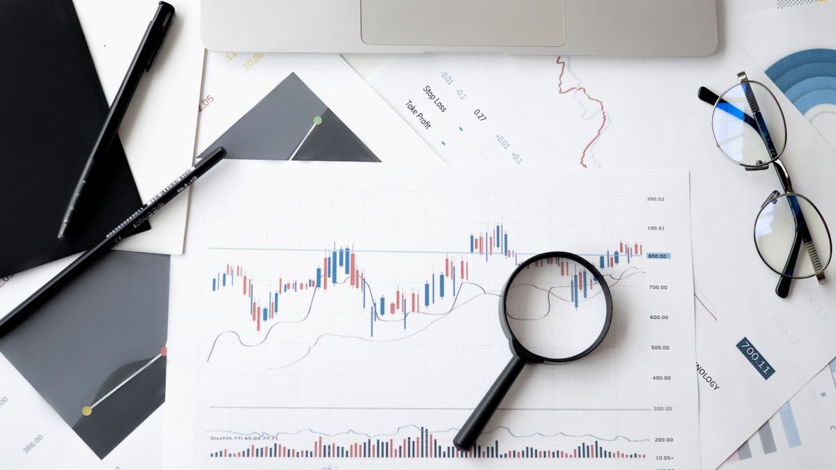 Mesa con gráficos financieros impresos, una lupa sobre un gráfico de velas, gafas, un bolígrafo y el borde de un portátil