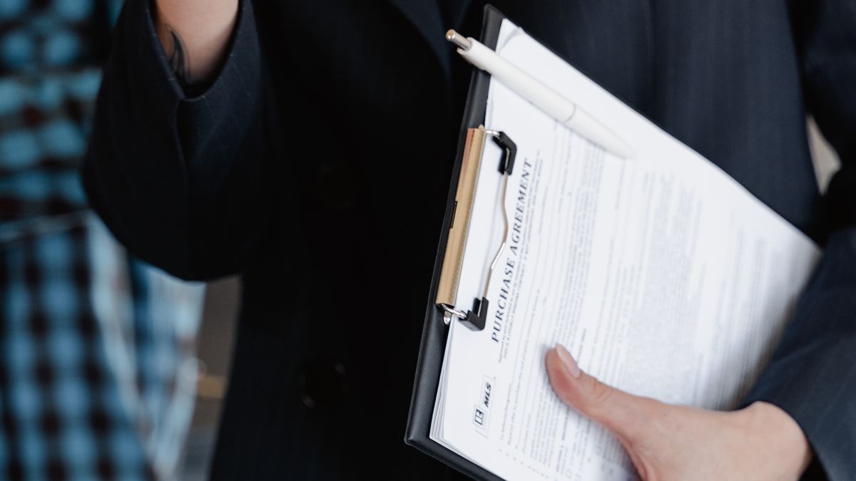 Persona con abrigo oscuro sosteniendo un portapapeles con un contrato de compraventa y un bolígrafo encima