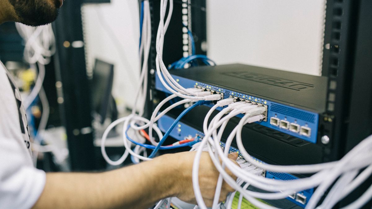Técnico manipulando un manojo de cables de red de colores conectados a un armario de comunicaciones