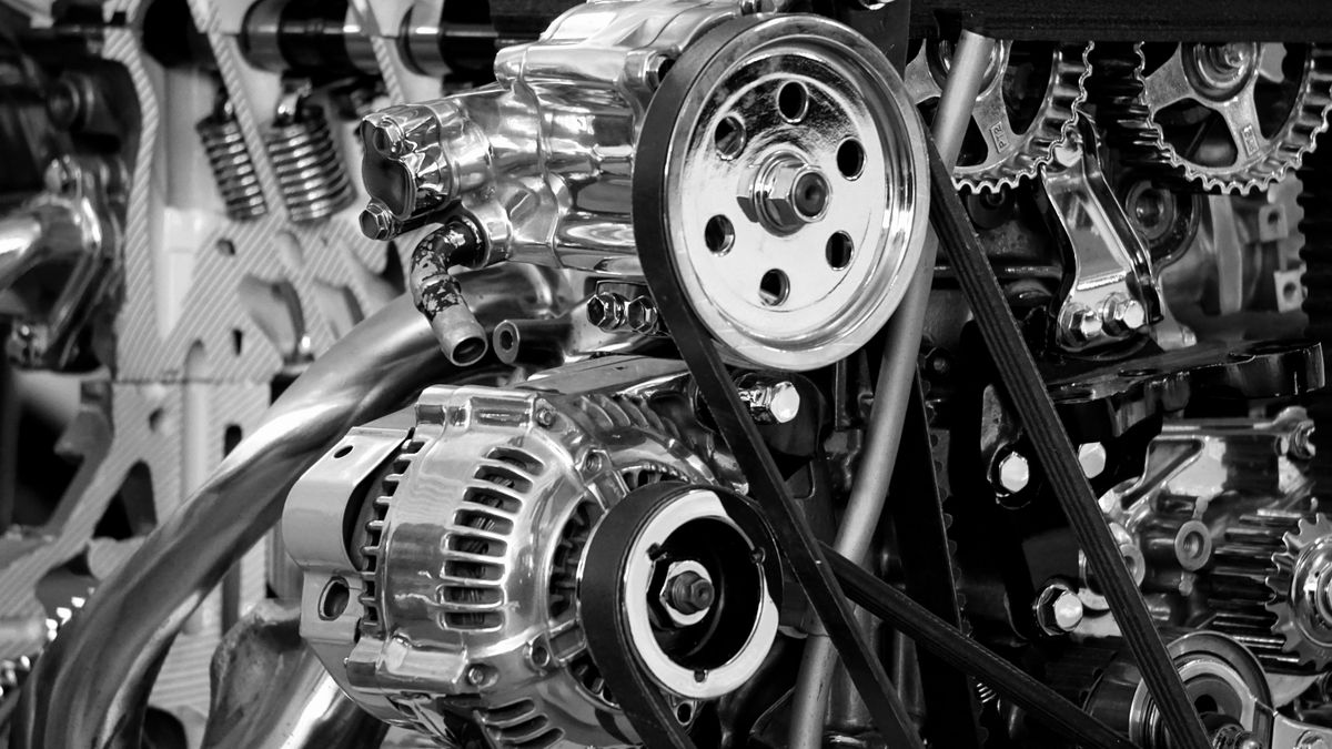 Black and white close-up of a stripped-down mechanical engine, with gears, pulleys and belts on show