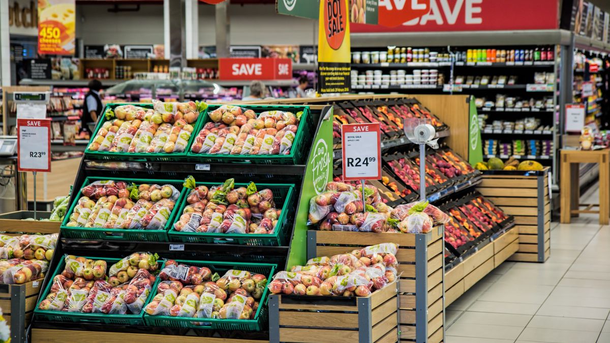 Pasillo de supermercado con cajas de fruta y carteles rojos de oferta con el precio escrito en grande