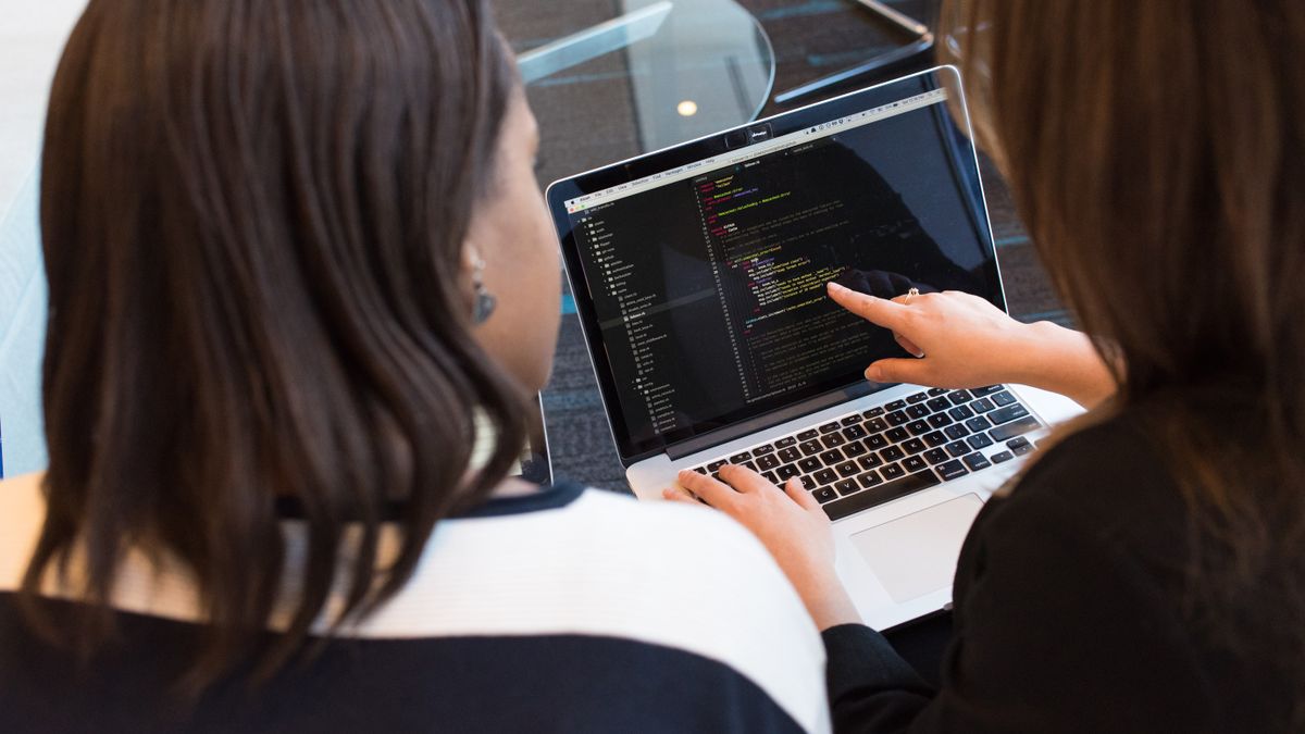 Two people reviewing lines of code together on a laptop screen, one pointing at a line with her finger
