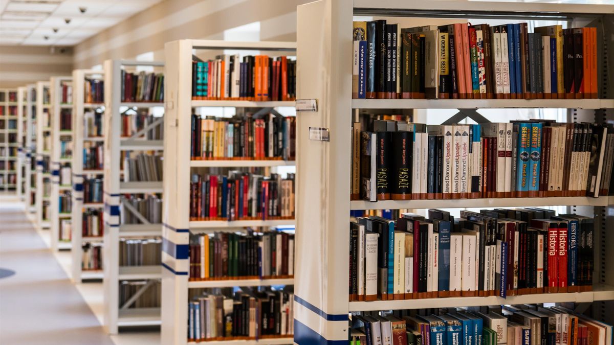 Pasillo de una biblioteca con estanterías metálicas llenas de libros ordenados y etiquetados
