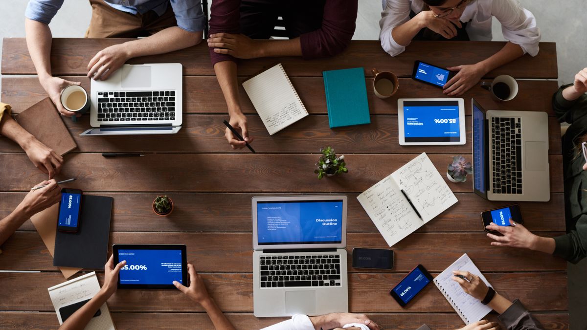 Overhead view of a wooden table surrounded by people with laptops, tablets and phones showing percentages and charts